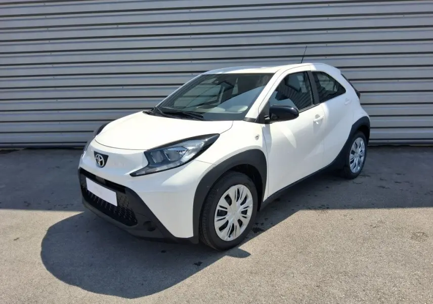Toyota Aygo X blanc pur vue 3/4 avant droit, avec protections noires autour des roues et rétroviseurs noirs.