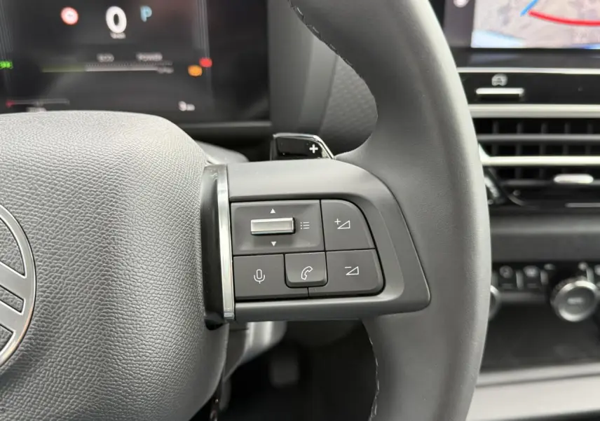 Gros plan sur les commandes au volant gauche du Citroën C4 blanc, avec affichage numérique en arrière-plan.