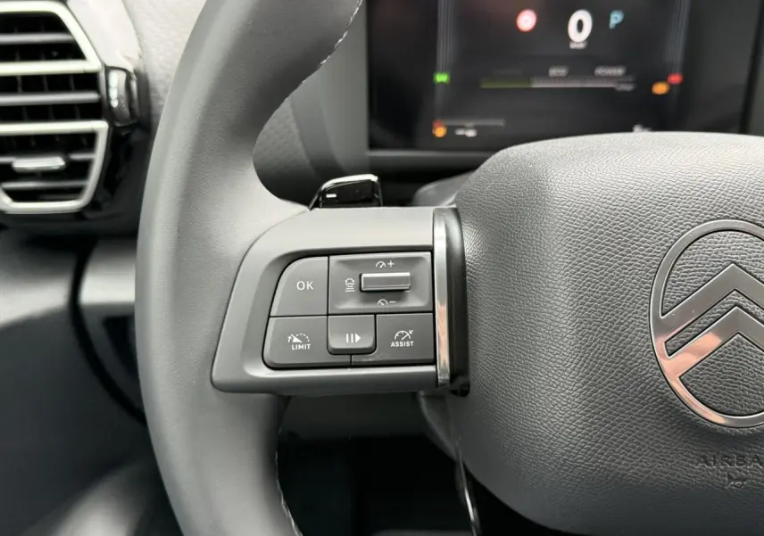 Gros plan sur le volant cuir gris du Citroën C4 2025 avec commandes intégrées et logo chromé au centre.