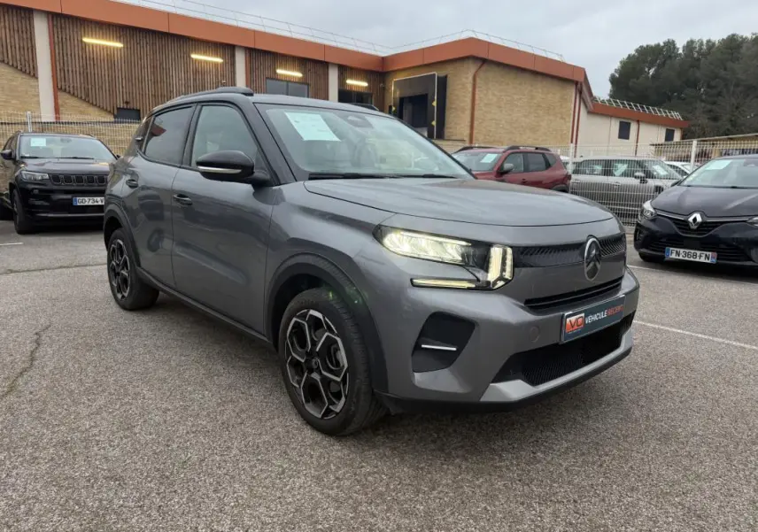 Vue 3/4 avant droit d'une Citroën C3 gris métallisé avec jantes alliage 17 pouces et barres de toit noires.