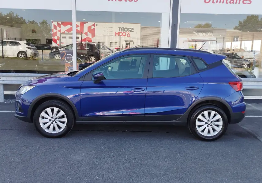 Vue de profil côté gauche d'une SEAT Arona bleu électrique avec jantes alliage et protections noires sur les bas de caisse.