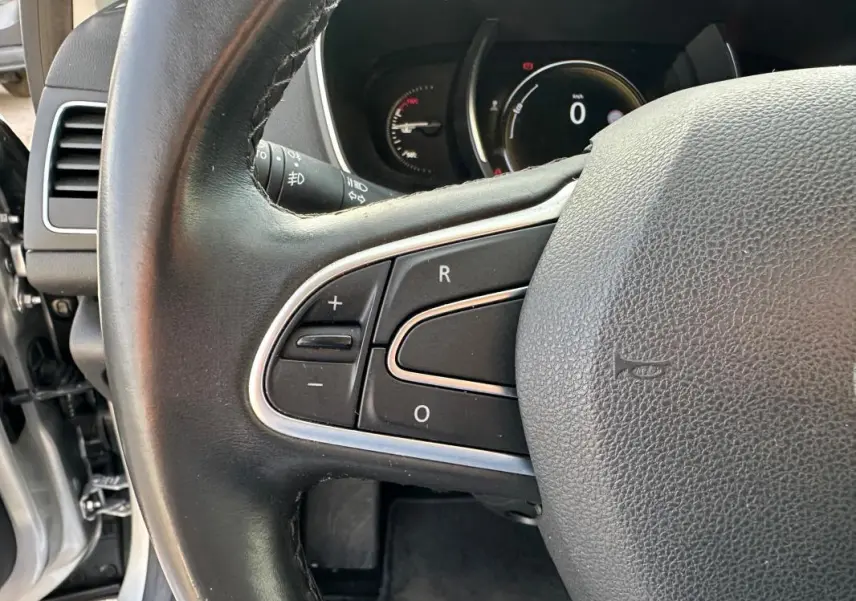 Gros plan sur le volant cuir noir de la Renault Mégane Break IV avec commandes intégrées côté gauche.