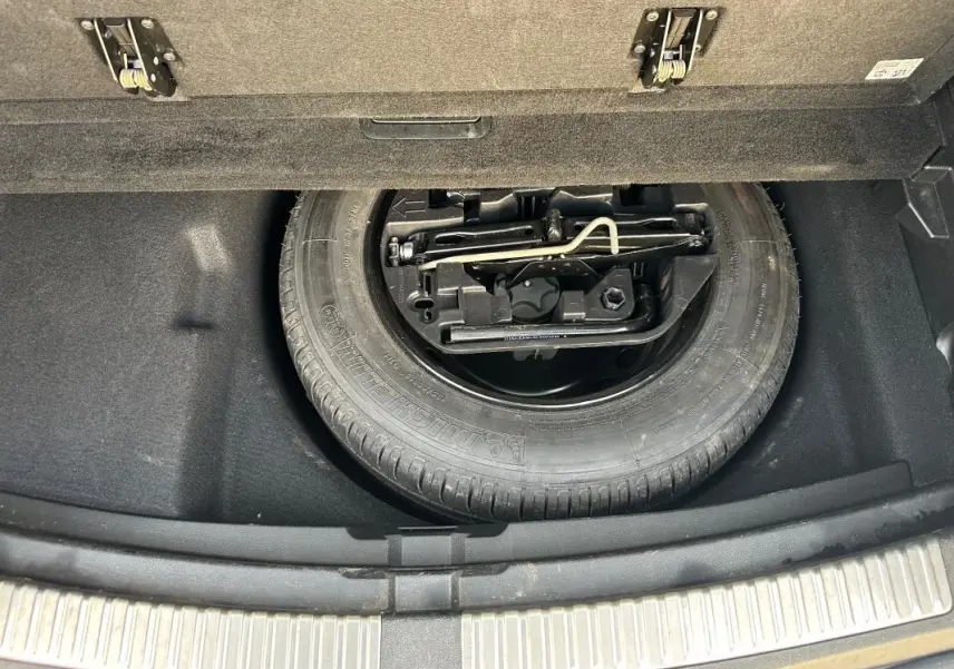 Roue de secours et outillage dans le coffre d'une Renault Mégane Break gris clair, vue plongeante sur le rangement.