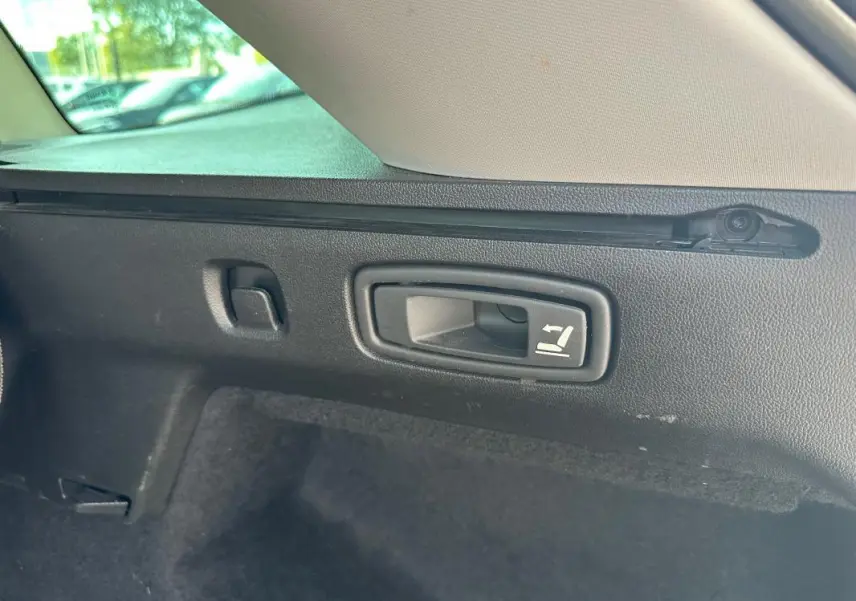 Gros plan sur la poignée de rabattement des sièges arrière dans le coffre d'une Renault Mégane Break gris clair.