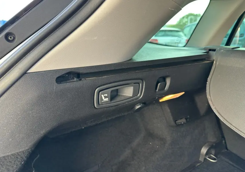 Détail de la commande de rabattement des sièges dans le coffre arrière de la Renault Mégane Break gris clair.