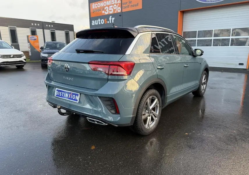 Volkswagen T-Roc bleu pétrole métallisé vu en 3/4 arrière droit avec attelage amovible sous la pluie.