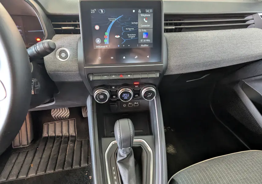 Vue intérieure de la Renault Clio hybride 2025 montrant la console centrale avec écran tactile, commandes clim et levier de vitesse.
