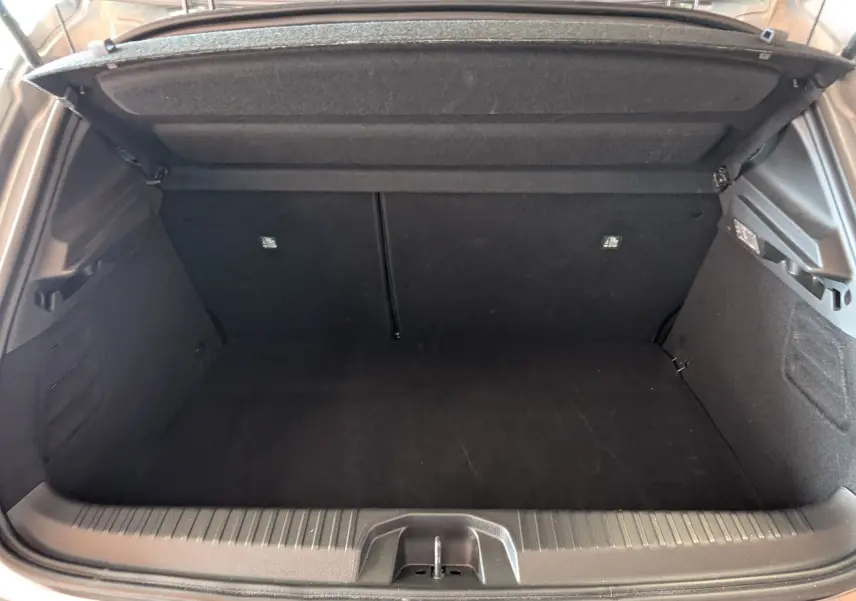Vue intérieure du coffre ouvert d'une Renault Clio V E-TECH Full Hybrid 145ch, tapis noir et habillage sombre visible.