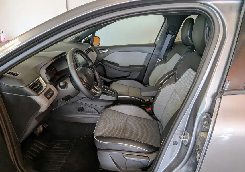 Vue intérieure côté conducteur de la Renault Clio gris schiste, sièges bi-matière gris et noir avec surpiqûres blanches.