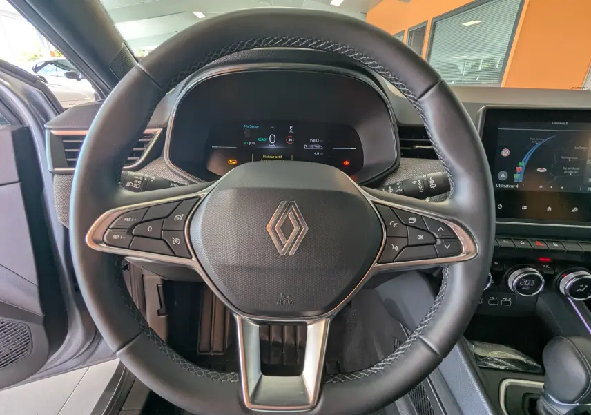Vue intérieure centrée sur le volant cuir noir de la Renault Clio hybride 2025 avec tableau de bord digital et écran tactile.