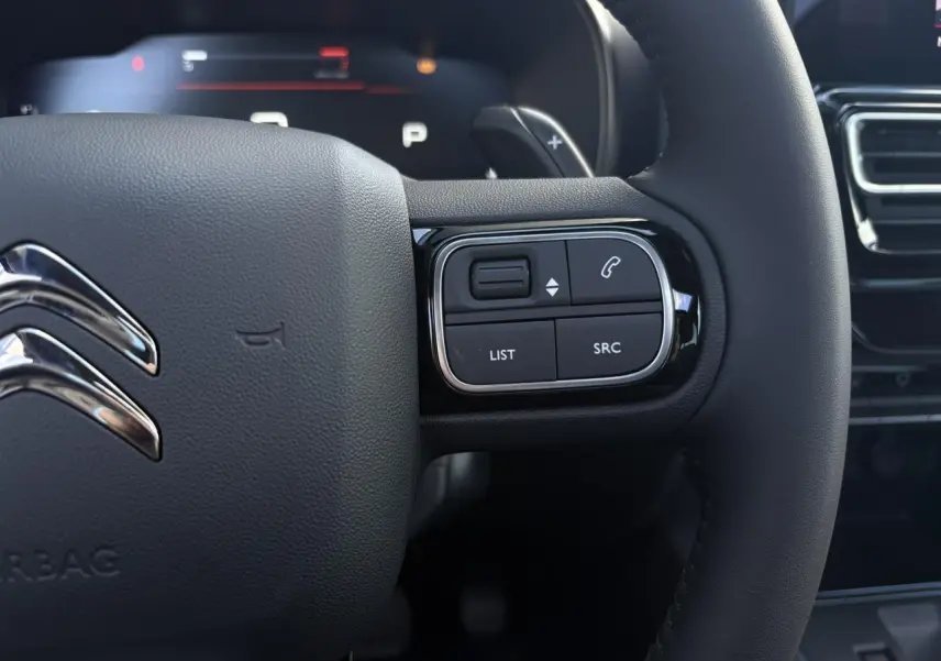 Gros plan sur le volant noir du Citroën C5 Aircross 2025, avec commandes intégrées et logo chromé visible.