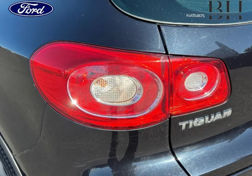 Feu arrière droit rouge sur Volkswagen Tiguan noir, gros plan sur le logo et la partie arrière du véhicule.