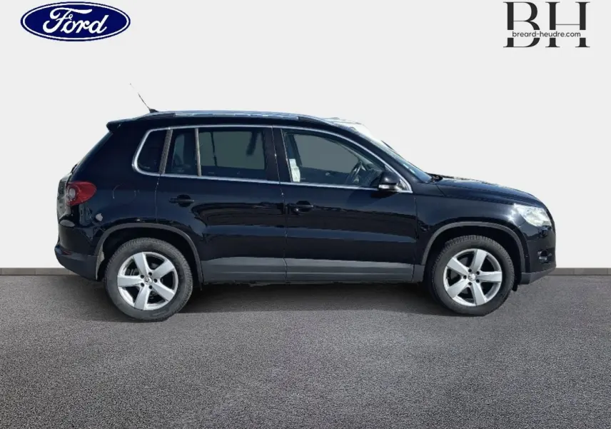 Profil côté gauche d'un Volkswagen Tiguan 2010 noir avec jantes alu et vitres teintées sur fond neutre.