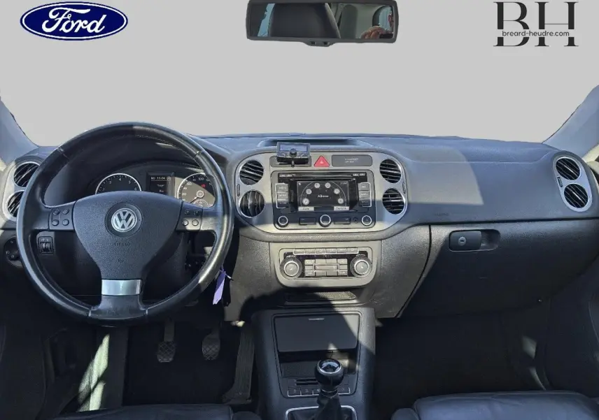 Vue intérieure avant du Volkswagen Tiguan beige 2010, volant cuir multifonction et tableau de bord avec écran central.