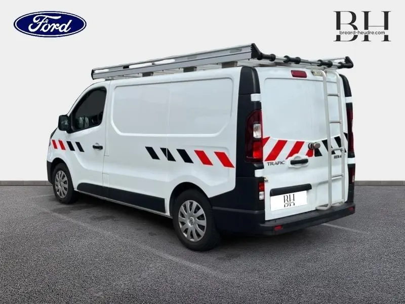 Renault Trafic Fourgon blanc glacier vu en 3/4 arrière droit avec galerie de toit aluminium et bandes de signalisation rouges et noires
