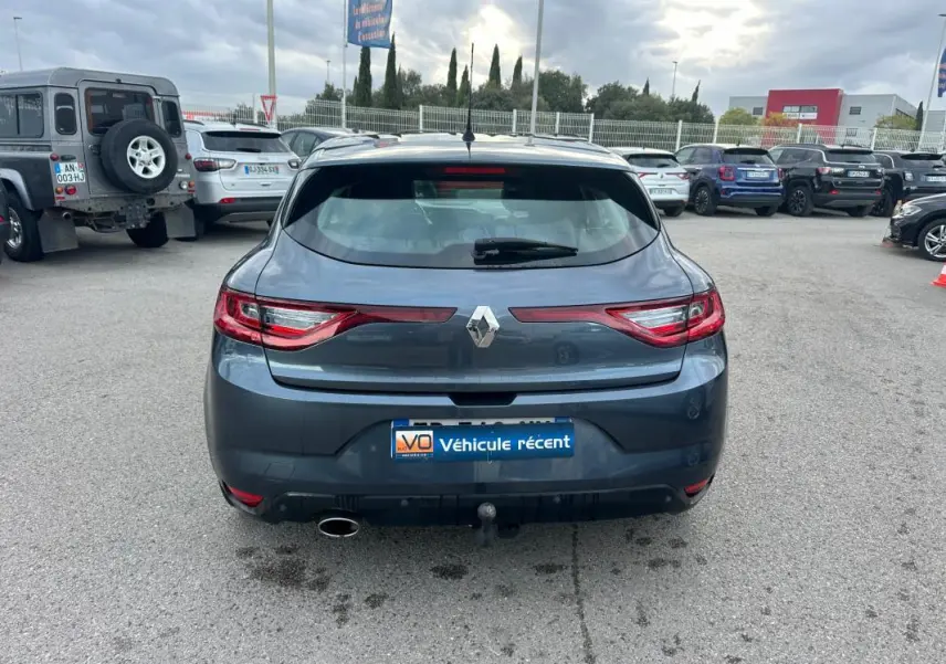 Vue arrière d'une Renault Mégane IV berline gris foncé avec feux LED et attelage de remorque visible sur parking.