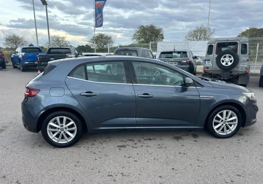 Profil côté gauche d'une Renault Mégane IV gris foncé, avec jantes alliage 18 pouces, garée en extérieur.