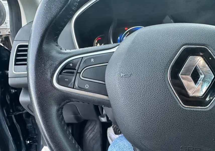 Gros plan sur le volant cuir avec commandes intégrées de la Renault Mégane IV gris foncé, tableau de bord en arrière-plan.