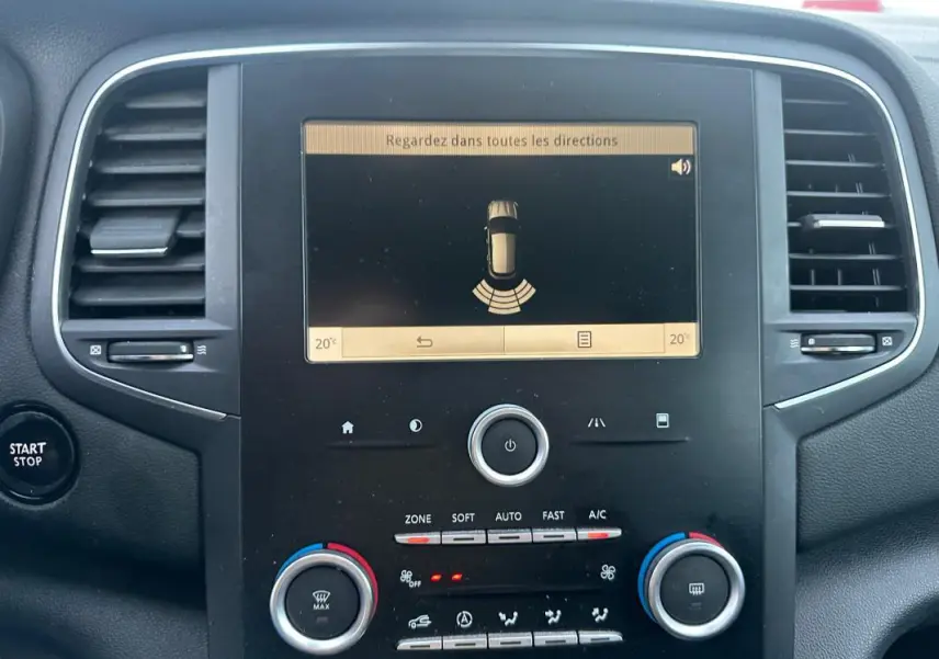 Vue rapprochée de la console centrale de la Renault Mégane IV gris foncé, affichant l'écran de détection d'obstacles et commandes climatisation.