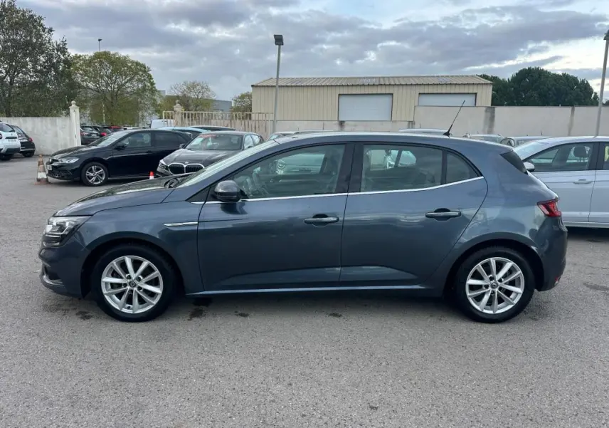Profil côté gauche d'une Renault Mégane IV gris foncé, jantes alliage 18 pouces, garée sur un parking extérieur.