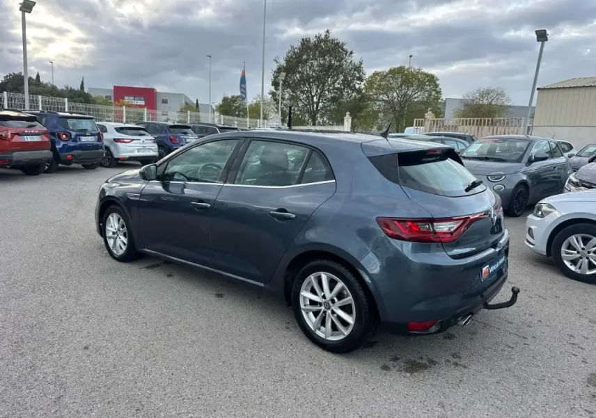 Renault Mégane IV gris foncé vue 3/4 arrière droit, jantes alliage 18 pouces et attelage visible en extérieur.