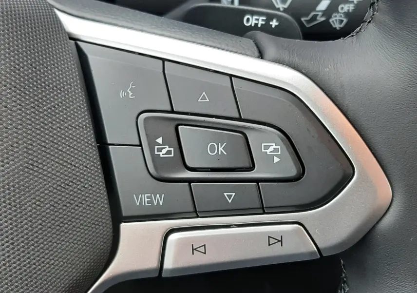 Gros plan sur les commandes multifonctions à gauche du volant cuir noir du Volkswagen T-Roc gris Pyrite 2025.