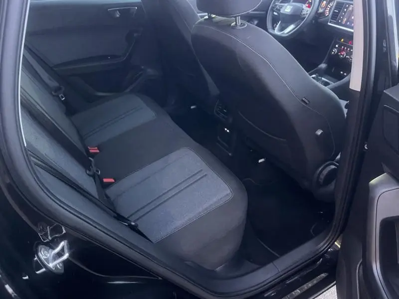 Vue intérieure côté arrière gauche du SEAT Ateca noir, montrant la banquette arrière et le siège avant avec tableau de bord partiellement visible.