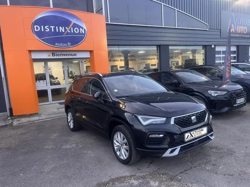 SEAT Ateca noir métal en 3/4 avant droit, garé devant un concessionnaire avec calandre chromée et jantes alu.