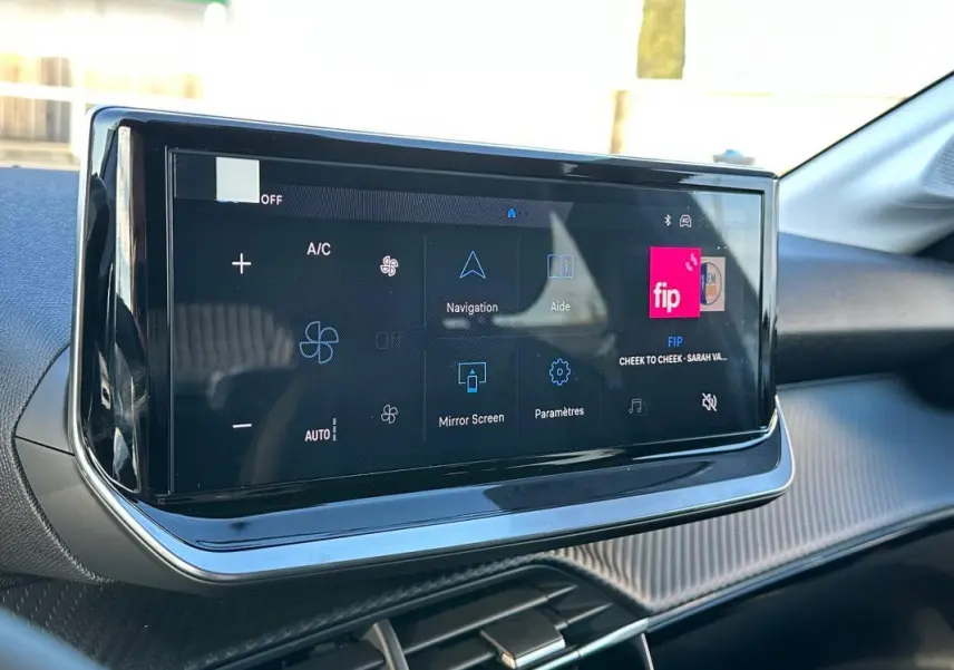 Écran tactile central du tableau de bord de la Peugeot 208 Hybrid blanc, avec commandes climatisation et navigation visibles.