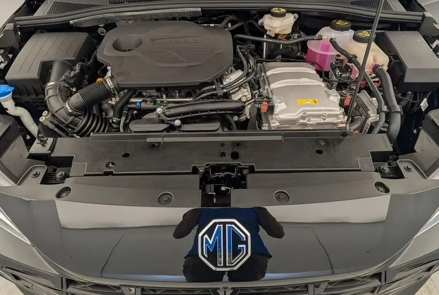 Vue plongeante sur le moteur hybride du MG3 Pebble Black, avec capot ouvert et logo MG visible sur la calandre noire.