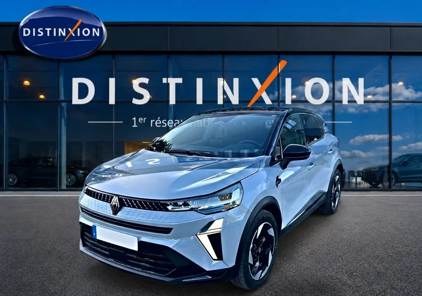 Vue 3/4 avant d'un Renault Captur gris rafale avec jantes noires et détails lumineux modernes, devant une vitrine Distinxion.