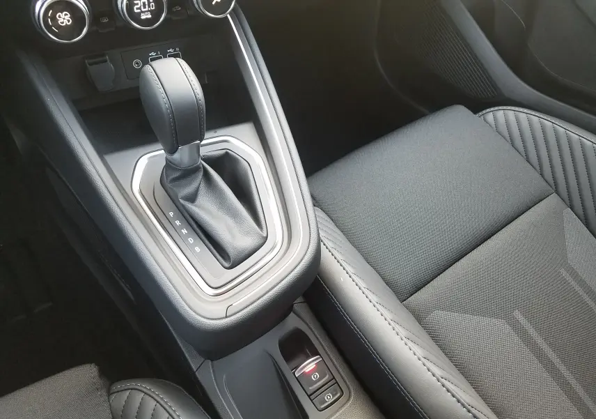 Gros plan sur la console centrale et le levier de vitesse automatique de la Renault Clio V gris Rafale, avec accoudoir noir et coutures bleues.