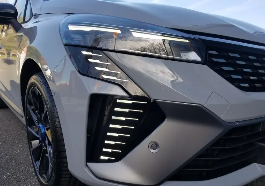 Gros plan sur l'avant gauche de la Renault Clio V gris Rafale, mettant en valeur ses phares LED et jante noire sportive.