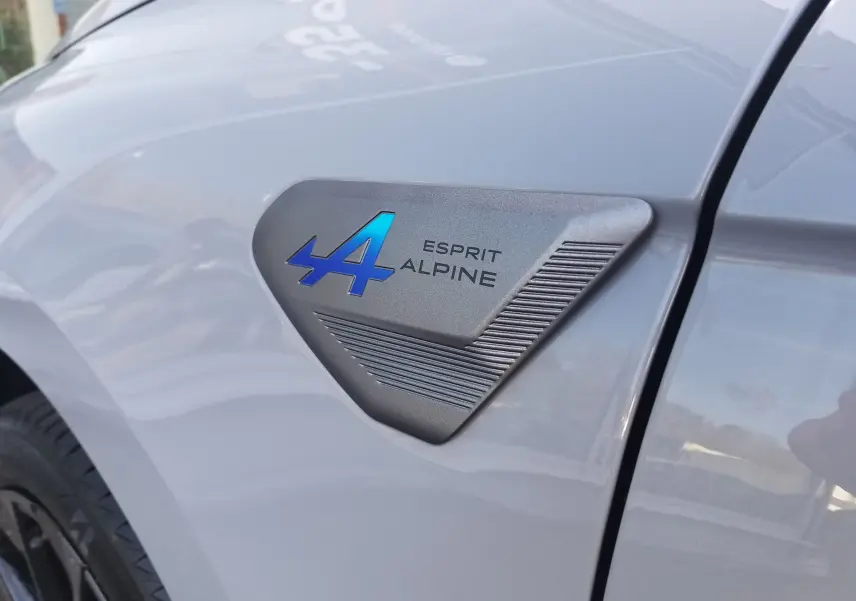 Gros plan sur l'écusson Esprit Alpine bleu sur l'aile avant gauche de la Renault Clio V gris Rafale.