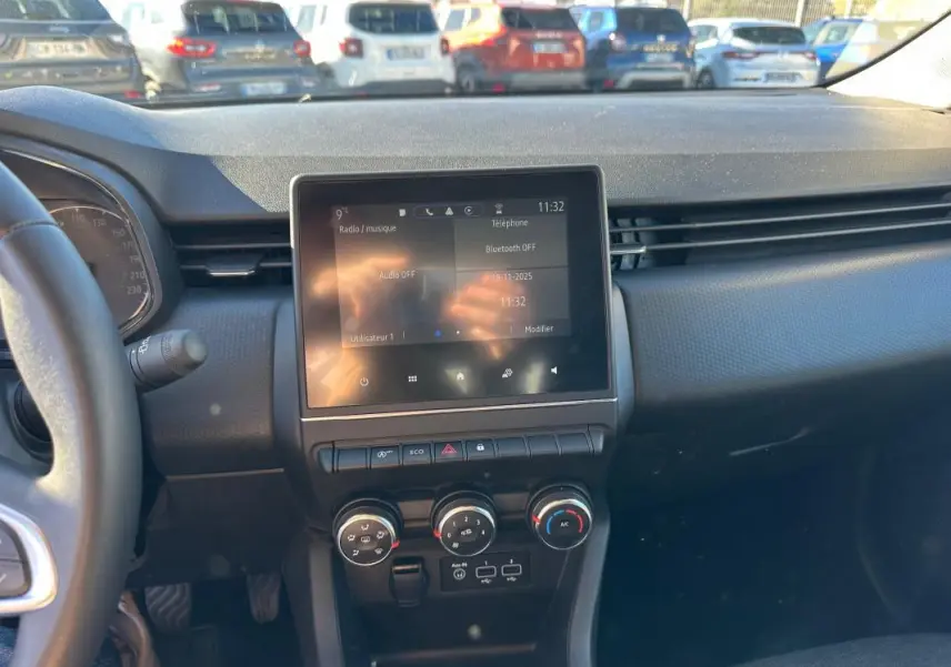 Vue intérieure du tableau de bord de la Renault Clio bleu foncé 2023, avec écran tactile central et commandes de climatisation manuelle.