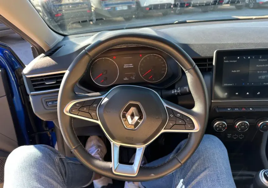 Vue intérieure centrée sur le volant de la Renault Clio bleu foncé 2023, avec tableau de bord et écran tactile visibles.