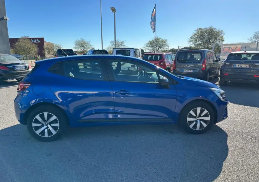 Profil côté gauche d'une Renault Clio V TCe 90 Équilibre bleu foncé garée en extérieur par temps ensoleillé.