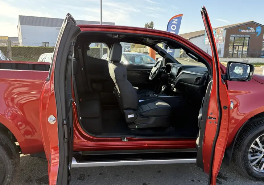 Vue latérale gauche du pick-up Isuzu D-MAX orange 2026 avec portes ouvertes et intérieur visible.