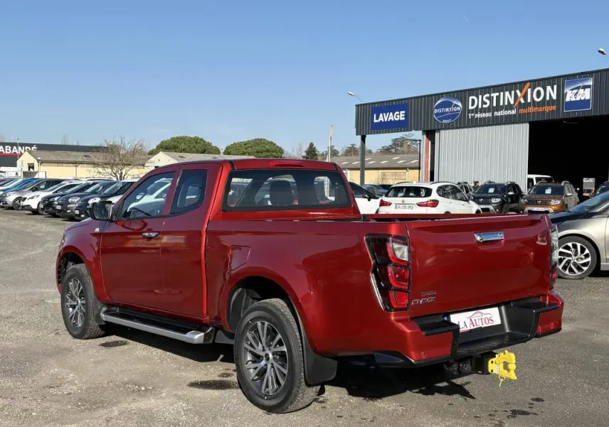 Vue 3/4 arrière droite d'un Isuzu D-MAX rouge métallisé avec jantes aluminium et attelage visible en concession.