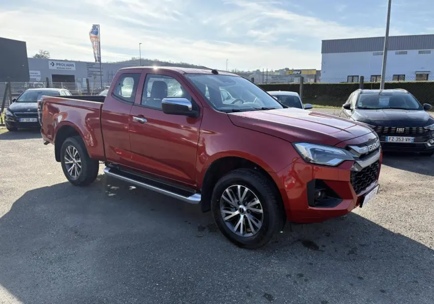 Isuzu D-MAX orange vue 3/4 avant droit, avec jantes aluminium et marchepieds latéraux visibles.