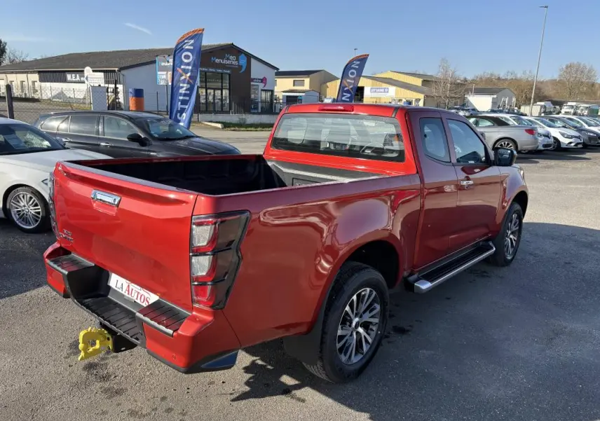 Vue 3/4 arrière droite d'un pick-up Isuzu D-MAX rouge avec benne ouverte et jantes aluminium sur parking.