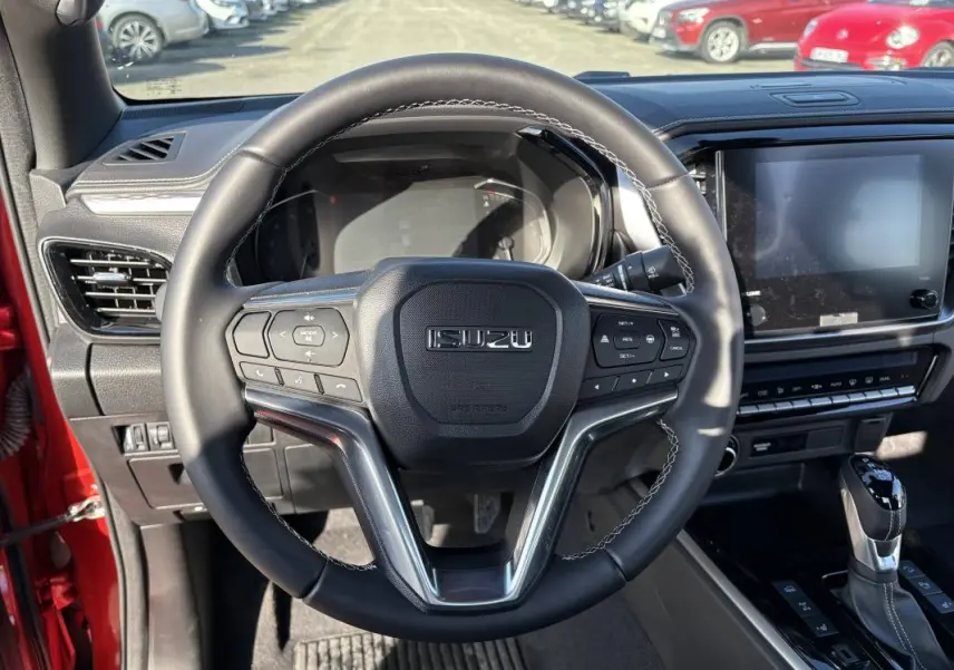 Vue intérieure centrée sur le volant multifonctions d’un Isuzu D-MAX orange avec tableau de bord et écran tactile.