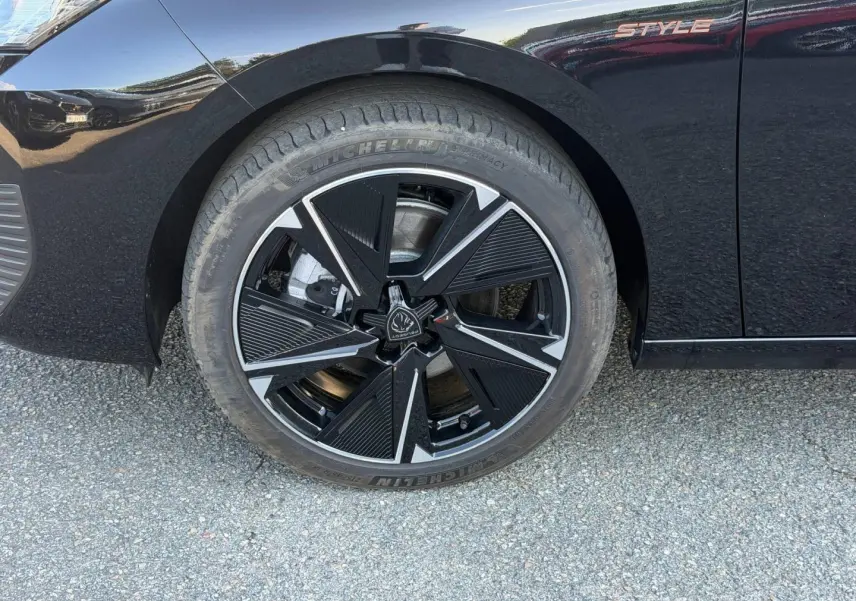 Gros plan sur la roue avant gauche noire et jante alu au design géométrique de la Peugeot e-308 Style noir Perla Nera.