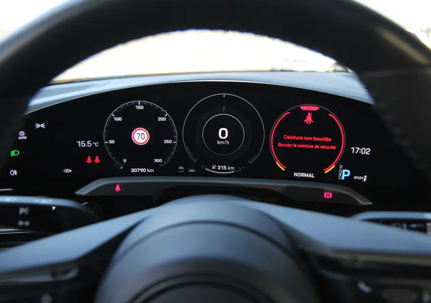 Tableau de bord numérique de Porsche Taycan Turbo gris anthracite, affichant vitesse, température et alertes ceinture.