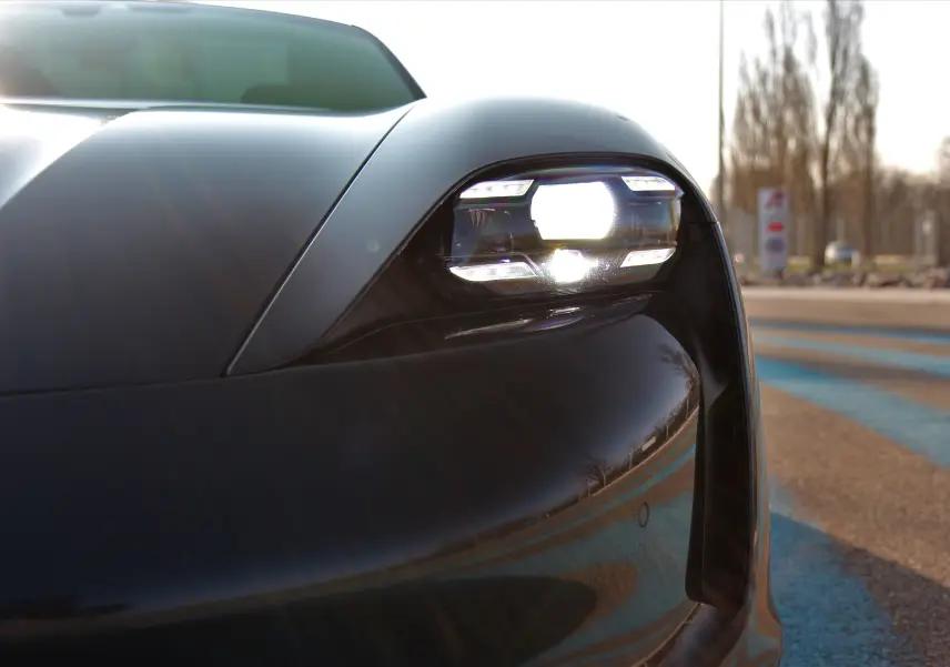 Gros plan sur le phare avant droit allumé d'une Porsche Taycan Turbo gris anthracite sous lumière naturelle.