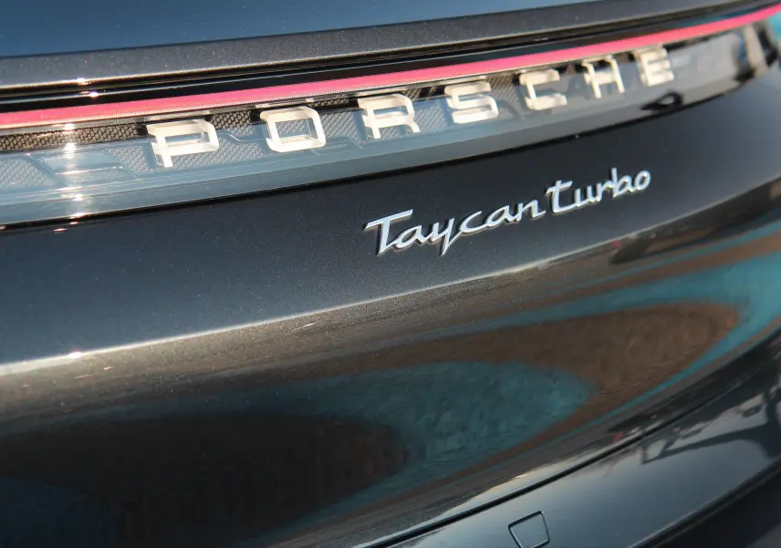 Gros plan sur l'arrière gris anthracite du Porsche Taycan Turbo avec logo et bande lumineuse rouge intégrée.