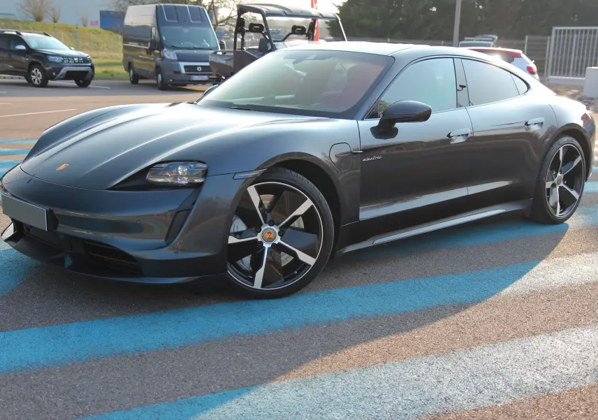 Porsche Taycan Turbo gris anthracite vue 3/4 avant droit, avec jantes exclusives et logo Porsche visible sur le capot.