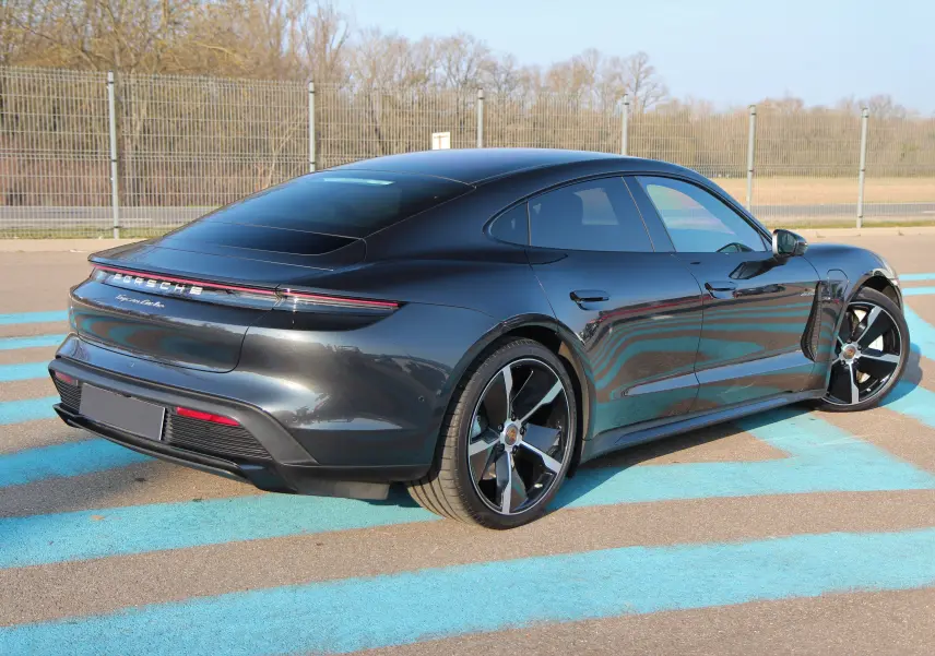 Vue 3/4 arrière droite d'une Porsche Taycan Turbo gris anthracite avec jantes exclusives 21 pouces sur parking.