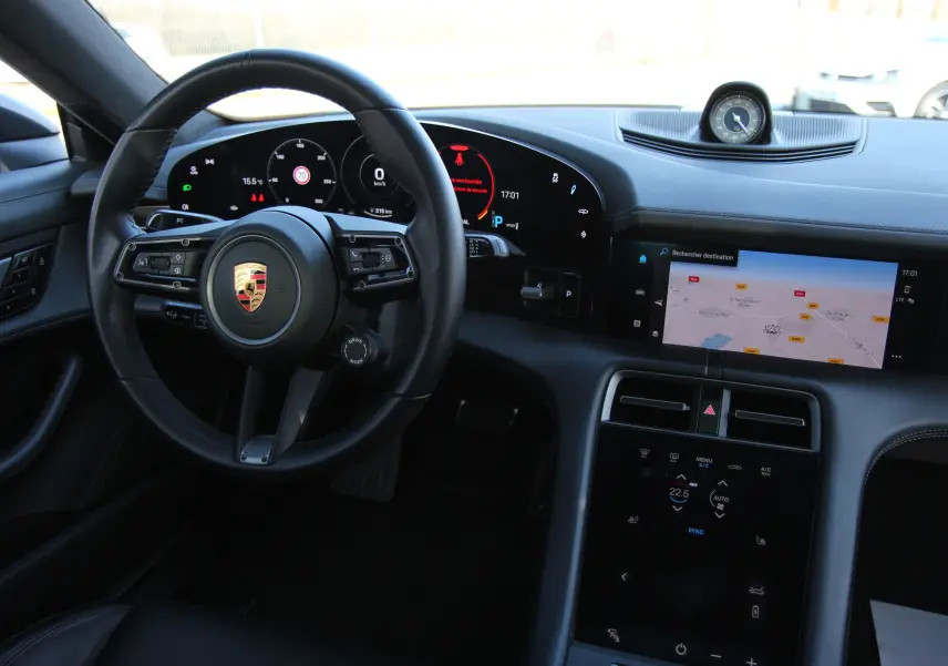 Vue intérieure du tableau de bord et volant cuir noir du Porsche Taycan Turbo 2020 avec écran tactile et horloge centrale analogique.