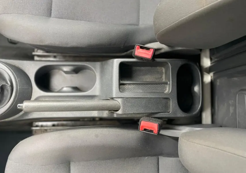 Vue plongeante sur la console centrale et les sièges avant gris du Volkswagen Caddy Van 2014, avec frein à main et ceintures rouges.
